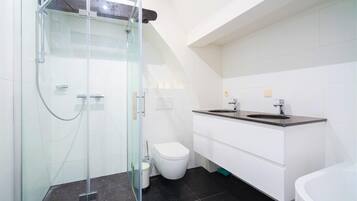 Une salle de bain moderne avec une douche à parois de verre, des toilettes blanches, un meuble-lavabo à deux vasques et une baignoire.
