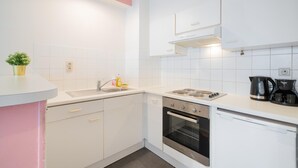 Une cuisine de taille réduite, avec des meubles blancs, un évier, une cuisinière, un four et un lave-vaisselle.