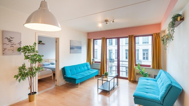 Un salon moderne avec un canapé bleu, une petite table, un luminaire suspendu et une plante en pot.