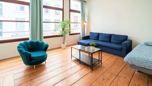 A room with a blue sofa, a teal armchair, a glass coffee table, and a potted plant. - Old town lodge Antwerp Apartment (Antwerp)