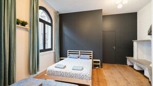 A bedroom with a bed, bedside tables, a window with curtains, a door, and a brick wall. - Spacious riverside apartment for 9 (Antwerp)