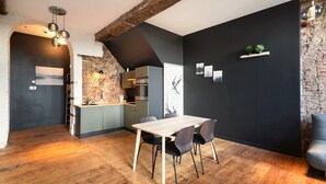 A modern kitchen with a brick wall, a dining area with a wooden table and chairs, and a black accent wall. - Spacious riverside apartment for 9 (Antwerp)