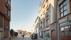 A cobblestone street with buildings, a Ferris wheel, and a cyclist. - Spacious riverside apartment for 9 (Antwerp)