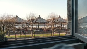 A view through a window of a building with traditional architecture, including a series of covered structures and a fenced outdoor area. - Spacious riverside apartment for 9 (Antwerp)