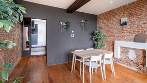 Un comedor con mesa y sillas de madera, pared de ladrillo y plantas colgantes.