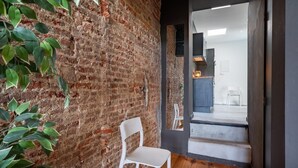 Una habitación con paredes de ladrillo visto, una silla blanca y un vano que da a otro espacio.