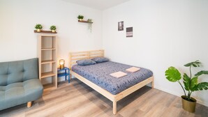 Un dormitorio con una cama, un sofá, un estante de madera y una planta en maceta.