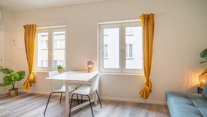 Una habitación moderna con una mesa blanca, dos sillas, un sofá azul y una ventana con cortinas amarillas.