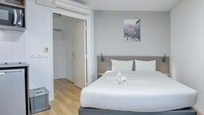 Ett hotellrum med en säng, en mikrovågsugn, ett litet pentry och en dörr som leder till ett annat rum.