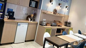A kitchenette with a microwave, toaster, and coffee machine, a small refrigerator, and a dining area with tables and chairs.