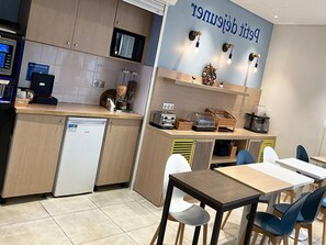 Eine Küchenzeile mit Mikrowelle, Toaster und Kaffeemaschine, einem kleinen Kühlschrank und einem Essbereich mit Tischen und Stühlen.