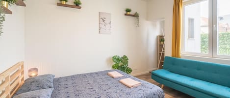 Ein Schlafzimmer mit einem Bett, einem blauen Sofa und Wandregalen mit Pflanzen.