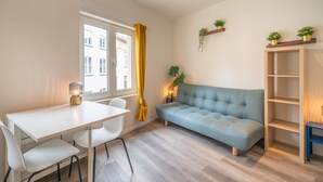 Uma sala de estar moderna com sofá, mesa de jantar, cadeiras, uma janela com cortinas amarelas e uma estante de livros.