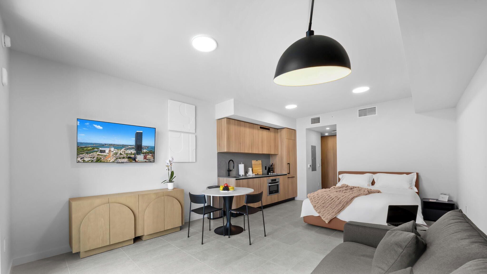 Een moderne hotelkamer met een bed, een bank, een eettafel met stoelen, een keukenhoek en een stadsgezicht op de muur.