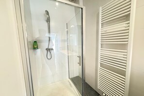 Eine gläserne Dusche mit Duschbrause, Handtuchhalter und einer grünen Flasche an der Wand.