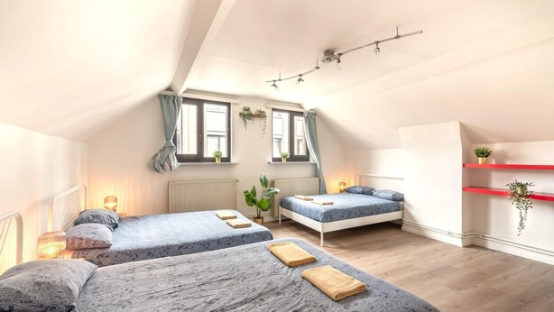 Ein Schlafzimmer mit zwei Betten, einem roten Regal mit Pflanze und einem Fenster mit Vorhängen.