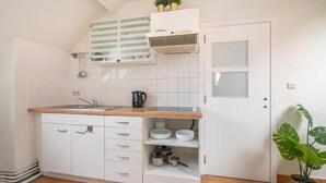 Eine kleine Küche mit weißen Schränken, einer Holz Arbeitsplatte, einem eingebauten Herd und einem Topf mit Pflanze.