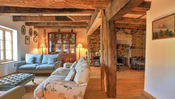 Un intérieur rustique avec des poutres apparentes, une cheminée et un coin salon confortable comprenant un canapé et un pouf.