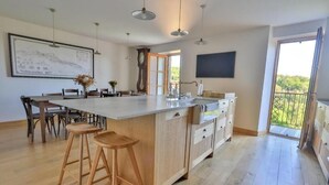 Une cuisine spacieuse dotée d’un grand îlot central, de planchers en bois, de luminaires suspendus et offrant une vue sur l’extérieur.
