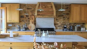 Une cuisine avec des meubles en bois, un mur en pierre, un grand îlot central et des luminaires suspendus.