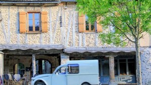 Une voiture ancienne est garée devant un bâtiment en pierre, sur lequel on peut lire l’inscription « Immo ».