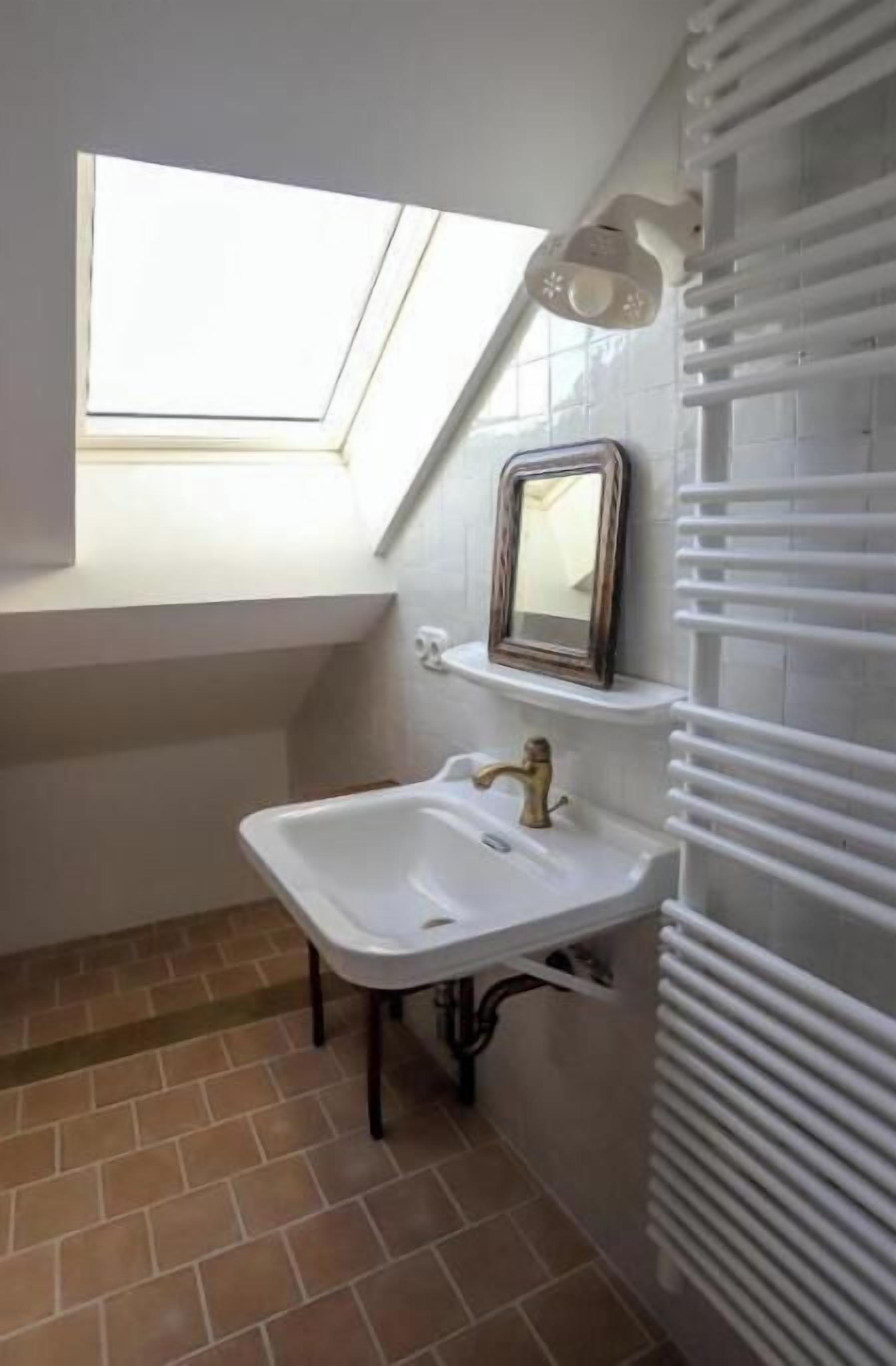 A small bathroom with a skylight, a white sink, a mirror, and a radiator.