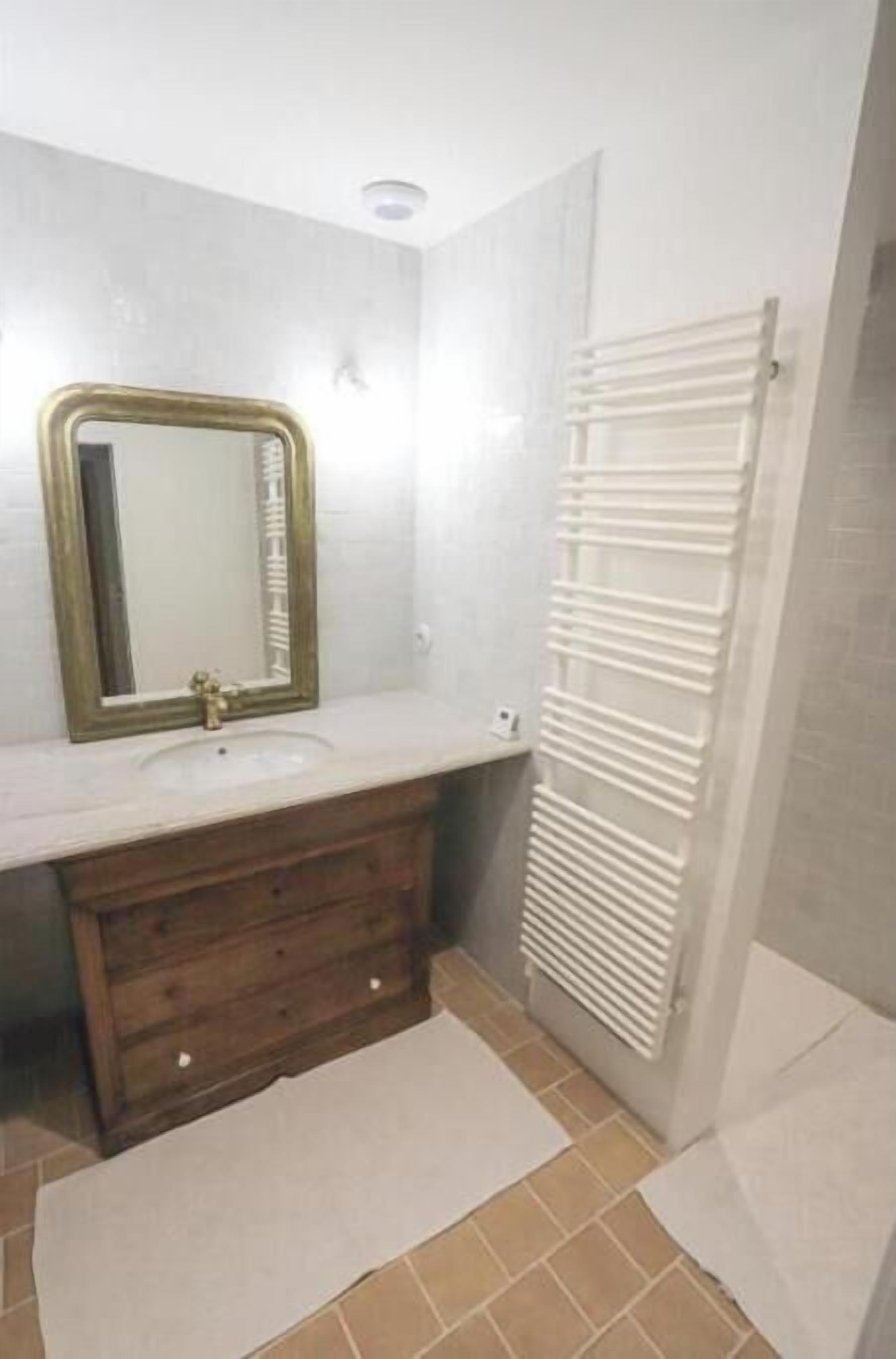 Ein Badezimmer mit einem Holzkosmetikschrank, einem Spiegel, einem weißen Waschbecken und einem Handtuchhalter.