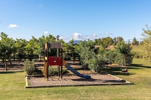 Ein Spielplatz mit Rutsche und Klettergerüst, umgeben von Bäumen und Gras.