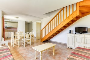 Ein Wohnzimmer mit einer Holztreppe, einem Essbereich und einer Küche im Hintergrund.