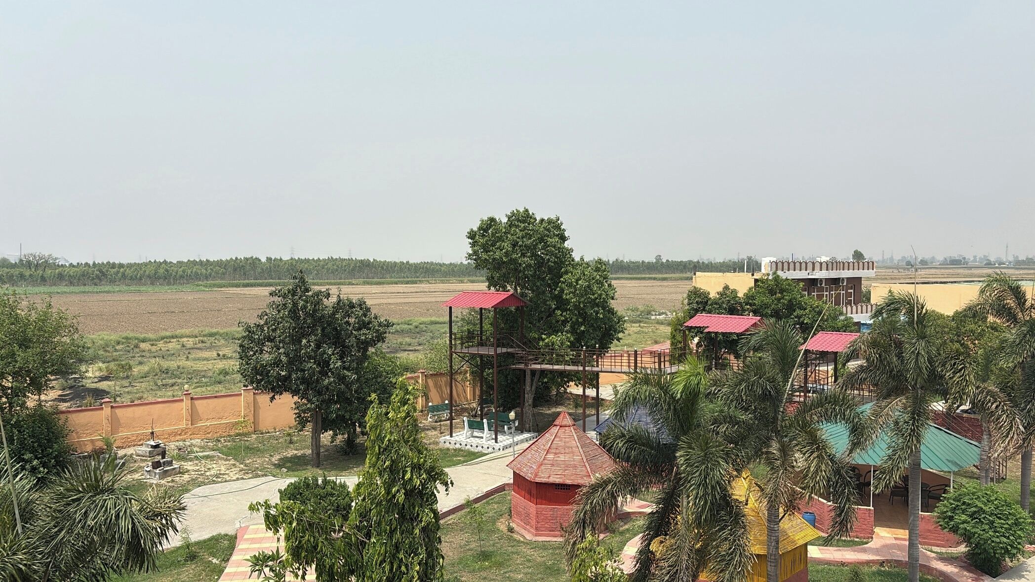 A rural landscape with a red-roofed pavilion, a yellow building, and a large tree.
