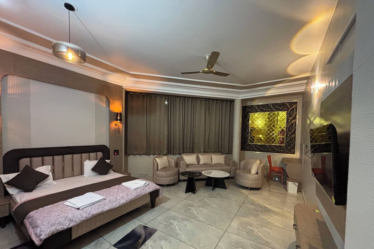 A modern hotel room with a bed, sofa, armchair, and a television.