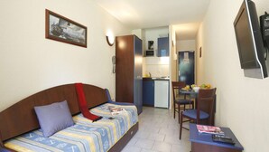Une pièce de taille modeste comprenant un canapé, une petite table, une chaise, un coin cuisine et un téléviseur.