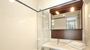 Une salle de bain dotée d’une douche à parois de verre, d’un meuble-lavabo en bois et d’un miroir au-dessus du meuble-lavabo.