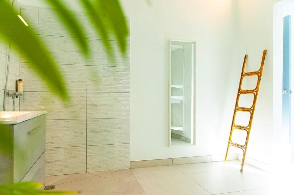Un baño con lavamanos blanco, espejo y una escalera de bambú.