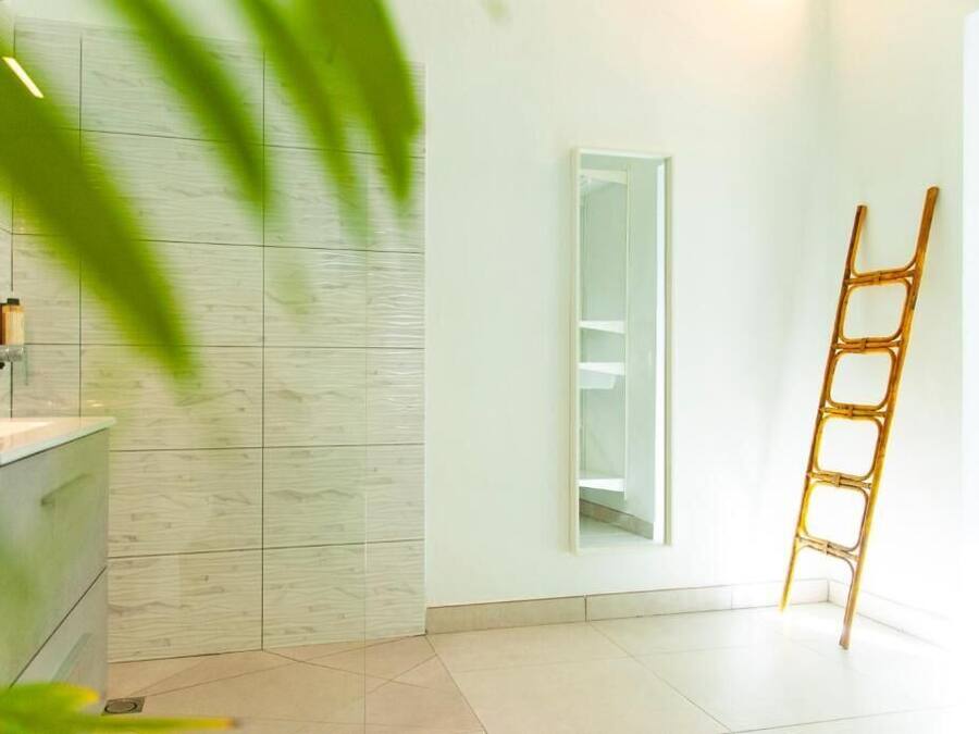 Un baño con lavamanos blanco, espejo y una escalera de bambú.