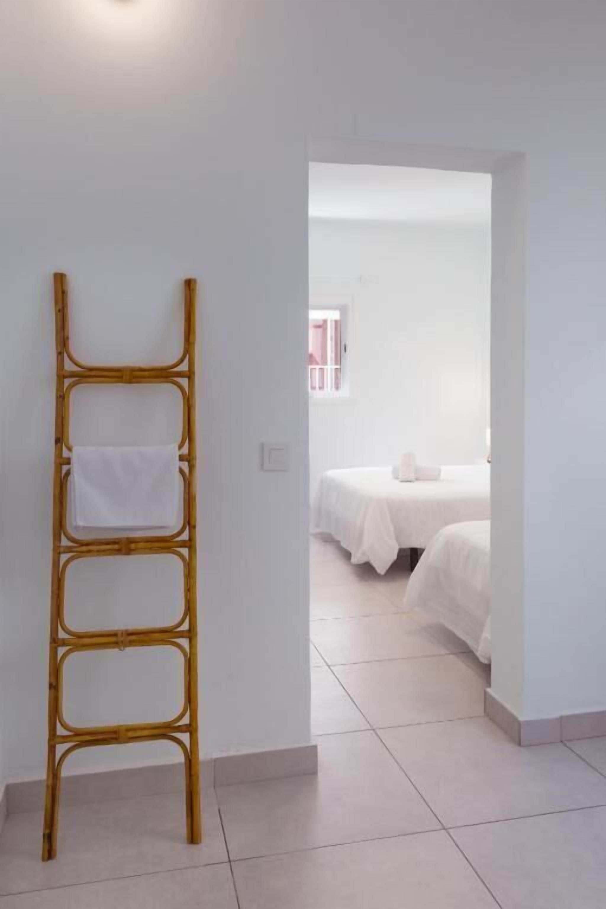 A room with a bamboo ladder leaning against a wall, a bed with white bedding, and a window with pink curtains.