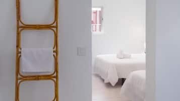 A room with a bamboo ladder leaning against a wall, a bed with white bedding, and a window with pink curtains.