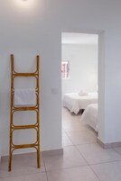 Una habitación con una escalera de bambú apoyada en una pared, una cama con ropa blanca y un ventanal con cortinas rosas.