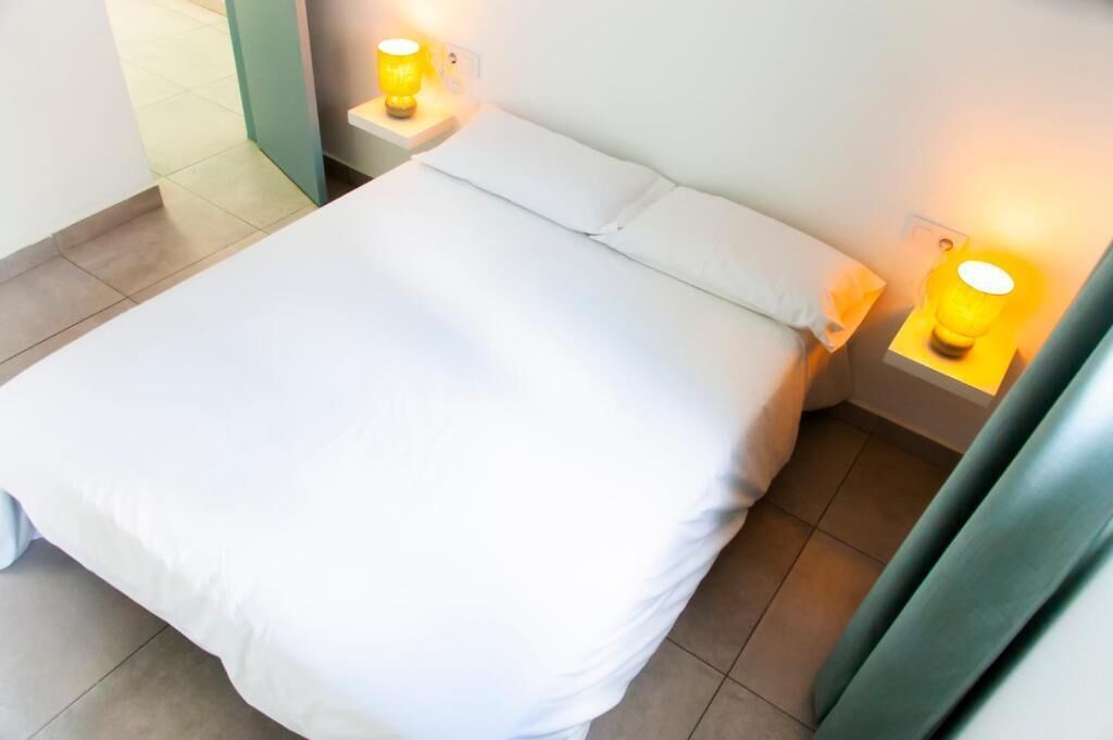 A bed with white bedding, two bedside lamps, and a plain wall.