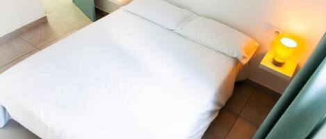 A bed with white bedding, two bedside lamps, and a plain wall.