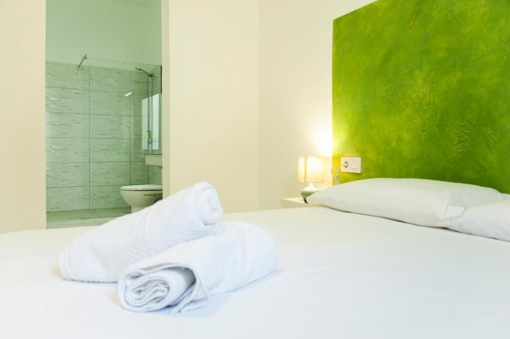 Ein Hotelzimmer mit Bett, einer grünen Akzentwand, einem Badezimmer mit Dusche und einem Nachttisch mit Lampe.
