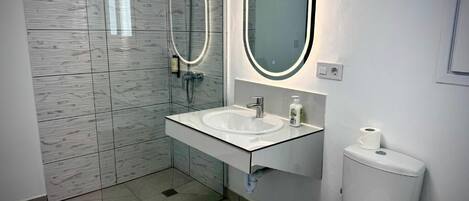 Ein modernes Badezimmer mit einer Duschkabine aus Glas, einem weißen Waschbecken mit Spiegel und einer Toilette.