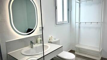 Un baño moderno con tocador con mampara de vidrio, inodoro y cabina de ducha.