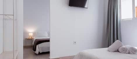 Habitación de hotel con cama, televisión montada en la pared, ventana con cortinas y una mesita de noche con lámpara.