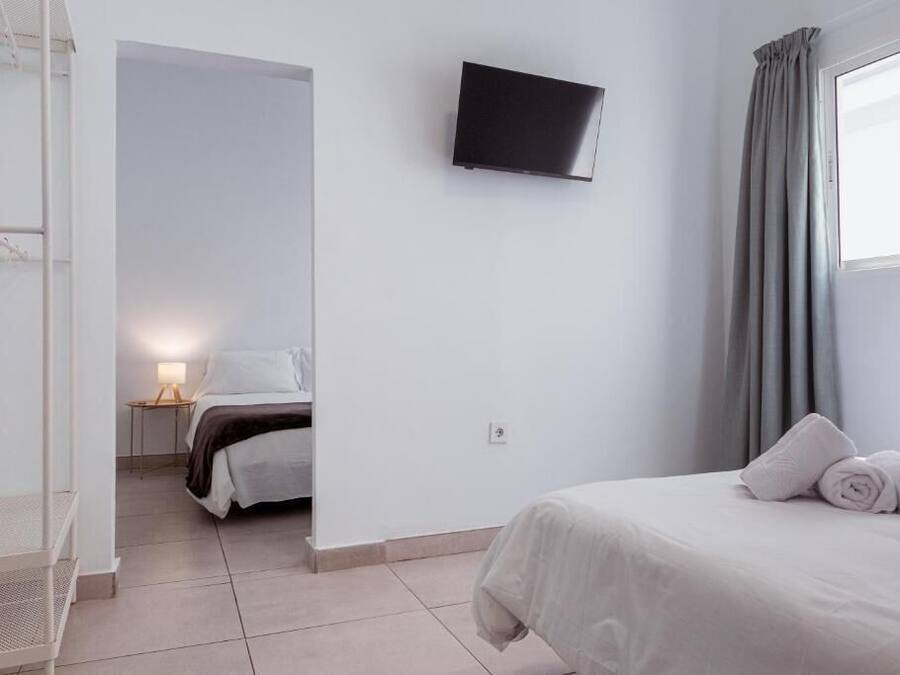 Habitación de hotel con cama, televisión montada en la pared, ventana con cortinas y una mesita de noche con lámpara.