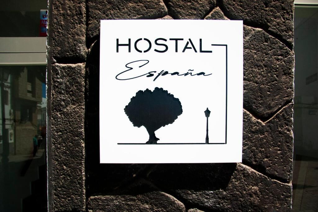 Et skilt med teksten 'HOSTAL España' og en silhuet af et træ samt en lygtepæl.
