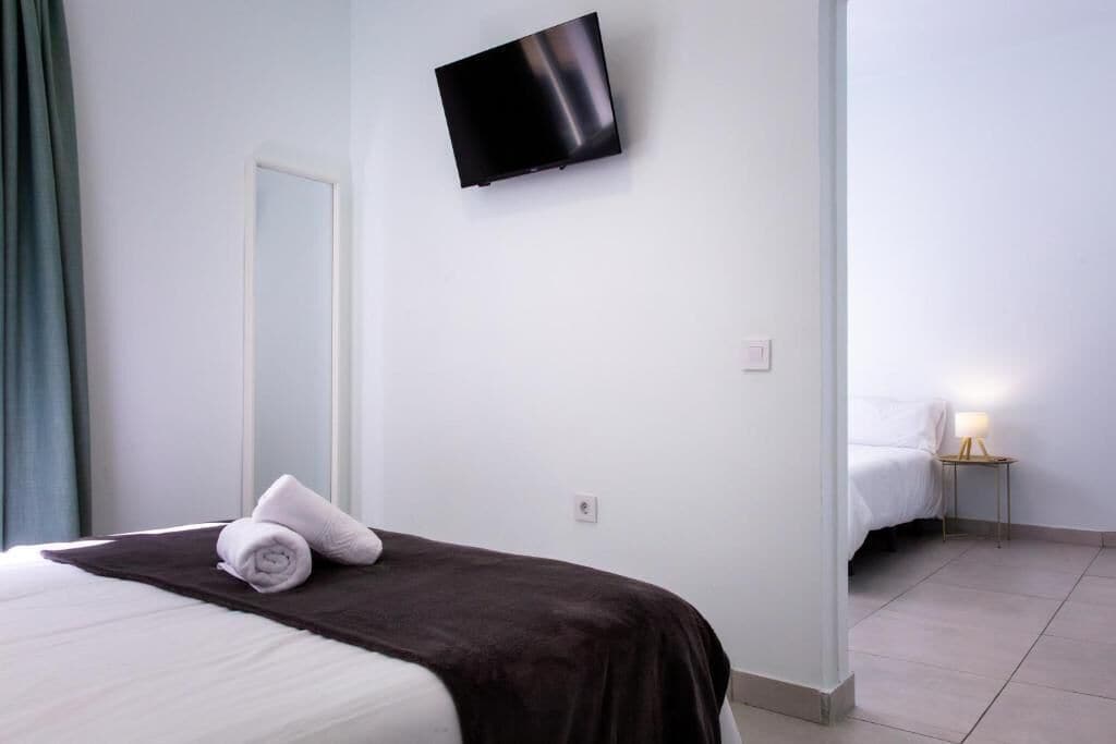 A hotel room with a bed, a TV mounted on the wall, a bedside lamp, and a mirror.