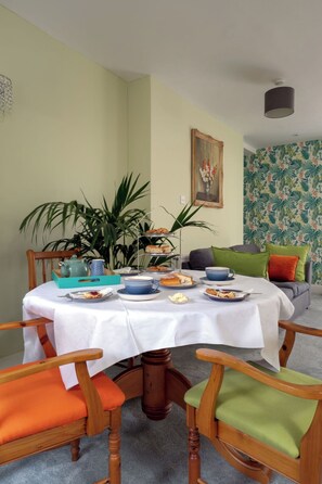 A dining area with a round table, chairs, a plant, a painting, and a patterned wall. - The Mews by Interhome (Torquay)