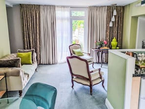 Ein Wohnzimmer mit einer Couch, Sesseln, einem Esstisch mit Blumen und Blick durch ein Fenster.