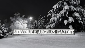 Paisagem nevada com uma placa que diz 'BIENVENUE à ARGELES GAZOST' e árvores cobertas de neve.